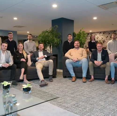 A group of professional individuals sat on sofas in a formal office setting posing for the photo.